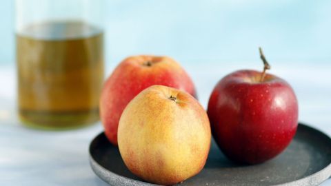 Drei Äpfel liegen auf einem Teller, während eine Glasflasche mit Apfelsaft im Hintergrund steht, bereit zur Nutzung.