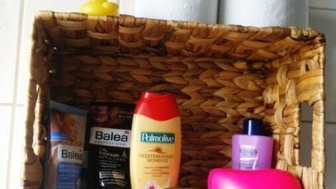 EinAufbewahrungskorb hängt an der Wand und hält Pflegeprodukte sowie Toilettenpapier in einem Badezimmer.