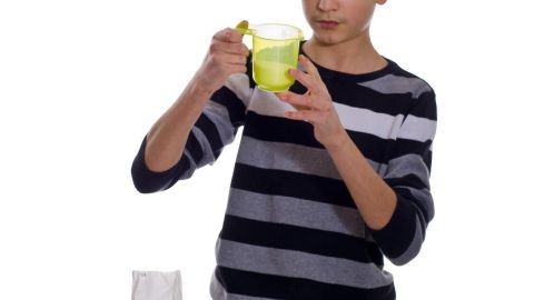 Ein Junge mit gestreiftem Shirt misst Zutaten in einem Messbecher, um Mengenverständnis beim Kochen zu fördern.