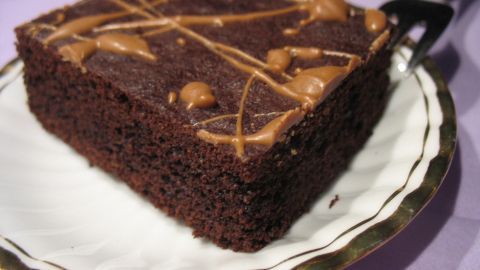 Ein saftiger Brownie liegt auf einem weißen Teller mit goldener Umrandung, umgeben von einem lilafarbenen Tisch.