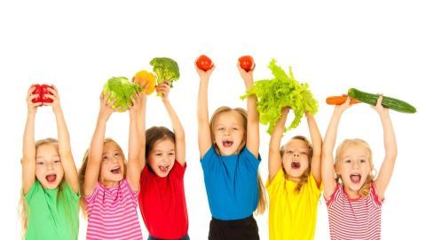 Sechs fröhliche Kinder halten begeistert bunte Gemüse hoch, um Gemüse für Kinder schmackhaft zu machen.