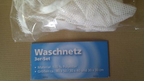 Ein Wäschenetz liegt zusammengefaltet auf einer Unterlage, bereit, Gardinen mit Röllchen zu schonen. Es ist in einer Verpackung.