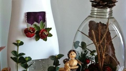 Ein kreatives Spielhaus aus einer leeren Flasche und einem Behälter zeigt eine dekorierte Szene mit Blumen und einer Figur.