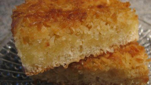 Saftiger Kokos-Bienenstich-Blechkuchen liegt auf einem eleganten Teller und strahlt mit seiner goldbraunen, knusprigen Oberfläche.