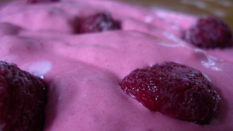Himbeer-Vegan-Eis mit frischen Himbeeren auf rosa-cremiger Oberfläche bietet eine verlockende Ansicht in Nahaufnahme.