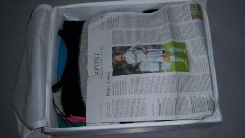 Ein Karton enthält Kleidung, die unter einer Zeitung liegt, um Kleidermotten zu vermeiden und die Textilien zu schützen.