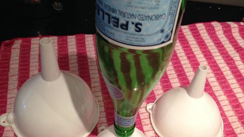 Ein grünes Getränkeglas mit engem Hals steht kopfüber auf einem weißen Trichter, um das Trocknen zu erleichtern.