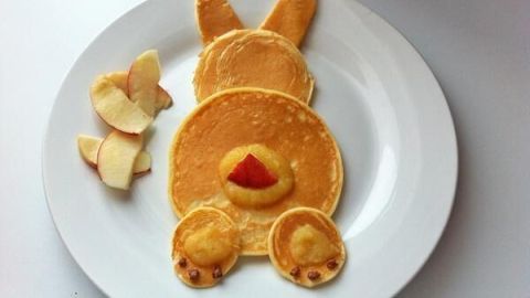 Ein Pfannkuchen-Hase liegt auf einem Teller, umgeben von Bananenscheiben, in kinderfreundlicher Form gestaltet.