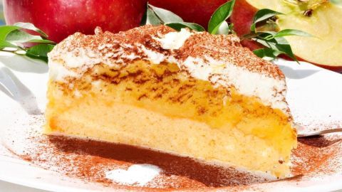 Ein saftiges Stück Apfelmus-Kuchen liegt auf einem Teller, umgeben von frischen Äpfeln und Sahne.