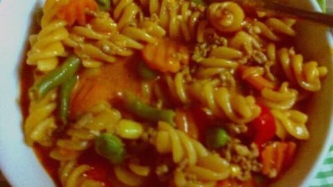 Ein Spirelli-Topf mit bunten Nudeln, Gemüse und Sauce wird appetitlich in einer Schüssel serviert.