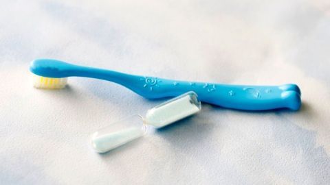 Eine blaue Zahnbürste liegt auf einem hellen Untergrund, daneben eine geöffnete Tube Zahnpasta, bereit zum Zähneputzen.