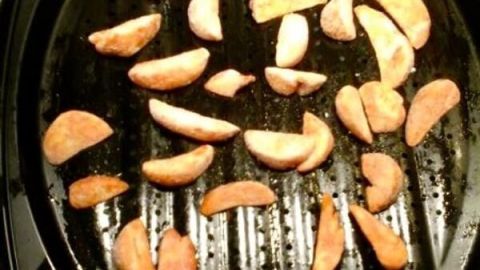 Knusprige, kalorienarme Pommes frittieren auf einem Grill, verteilt auf einer schwarzen Grillplatte in einer Küche.