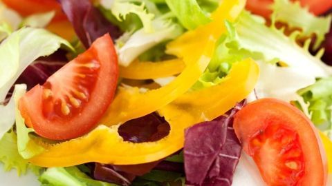 Ein frischer Salatteller mit knackigem Gemüse, darunter Tomaten, gelbe Paprika und verschiedene Salatblätter, liegt auf einem weißen Teller.