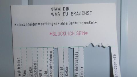 Eine Postkarte hängt an einer Wand und fordert dazu auf, Dinge zu nehmen, die man braucht, in einem einladenden Kontext.