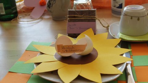 Ein liebevoll gedeckter Tisch zeigt einen bunten Teller mit einer Sonnenblume und dekorierten Eiern für das Osterfrühstück.
