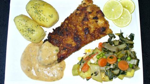 Fisch-Cordon bleu auf Teller mit Petersilienkartoffeln, gemischtem Gemüse und Zitronenscheiben in heller Soße angerichtet.