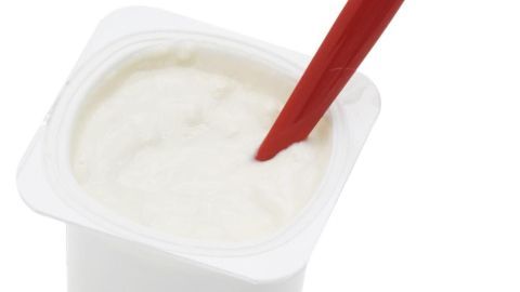 Ein Becher mit cremigem Kuchenmix steht auf einem Tisch, während ein roter Löffel darin steckt.