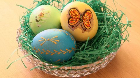 Bunte Ostereier liegen in einem grünem Nest aus Papier, dekoriert mit Serviettentechnik und Motiven wie einem Schmetterling.