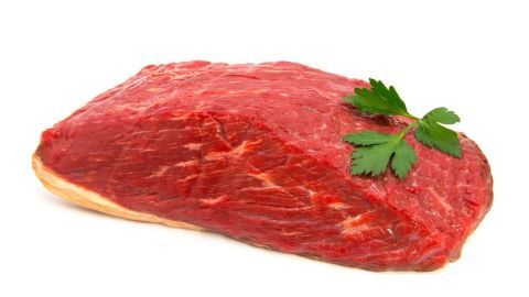 Ein Stück rohes Fleisch liegt auf einem weißen Untergrund und wird mit frischer Petersilie garniert.
