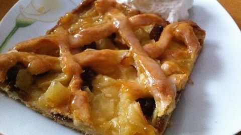 Ein Stück Apfelkuchen mit Gitter liegt auf einem Teller, dekoriert mit Sahne, in einer gemütlichen Küche.