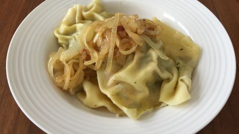 Leckere Maultaschen liegen auf einem weißen Teller, garniert mit gedünsteten Zwiebeln, auf einem Holztisch.
