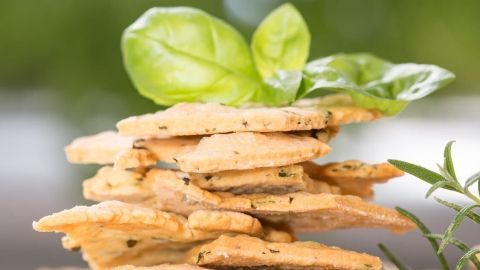 Zwiebelplätzchen liegen gestapelt auf einem Teller, umgeben von frischen Kräutern und einer grünen Pflanze im Hintergrund.