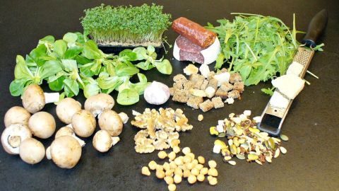 Frische Salattoppings liegen ansprechend angeordnet auf einer dunklen Fläche und laden zur Zubereitung eines Salats ein.