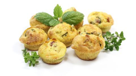 Saftige Muffins liegen gruppiert auf einem weißen Hintergrund, umgeben von frischen Kräutern, bereit zum Genießen.