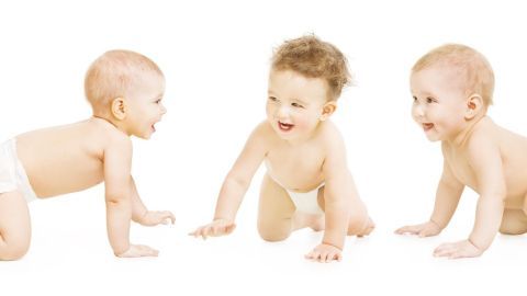 Drei fröhliche Babys krabbeln auf einem weißen Untergrund, erkunden neugierig ihre Umgebung und spielen miteinander.