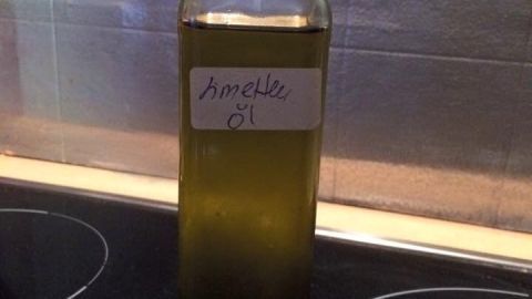 Eine Flasche mit grünlichem Öl steht auf einem schwarzen Kochfeld, beschriftet mit "Smeille Öl".