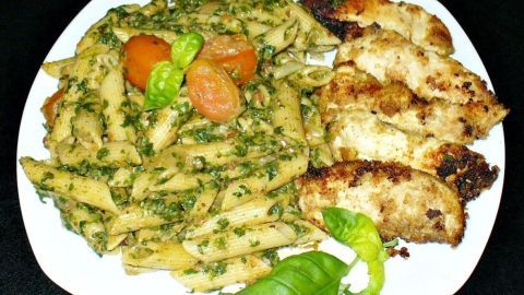 Krosse Hähnchenschnitzel liegen neben Knoblauchnudeln, umgeben von frischem Spinat und Gemüsestücken auf einem weißen Teller.