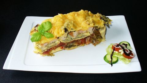 Eine appetitliche Maultaschen-Lasagne liegt auf einem weißen Teller, umgeben von dekorativem Gemüse und Sauce.
