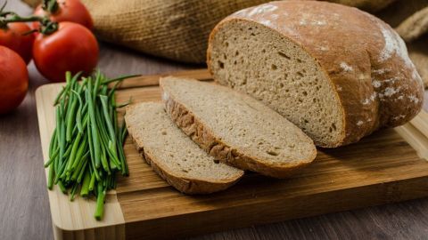 Schnittbrot liegt auf einem Holzbrett, umgeben von Frühlingszwiebeln und frischen Tomaten in einem rustikalen Ambiente.