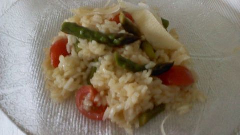 Ein Teller mit cremigem Risotto, verfeinert mit grünem Spargel und Kirschtomaten, auf einem dekorativen Glasuntergrund.