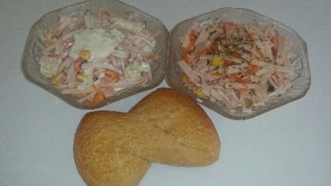 Zwei Schalen mit Wurstsalat stehen neben einem Brötchen auf einer weißen Oberfläche, bereit zum Genießen.