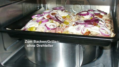 Ein Backblech mit Gemüse und Käse befindet sich in einer Mikrowelle, während es zum Backen ohne Drehteller genutzt wird.