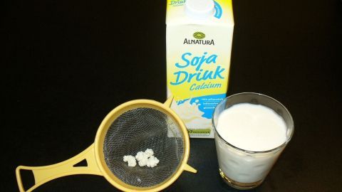 Sojamilch und ein Glas Kefir stehen auf einem Tisch. Die Sojamilch wird vorbereitet, um laktosefreien Kefir herzustellen.