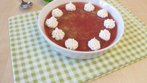 Eine Schüssel Rhabarbergrütze, dekoriert mit Sahnehäubchen, liegt auf einem karierten Tischcloth aus Baumwolle.