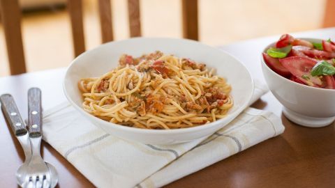 Eine Schüssel mit Spaghetti in schneller Thunfischsoße steht auf einem Tisch, daneben eine Schüssel mit frischem Salat.