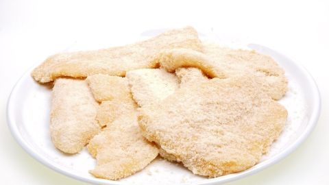 Panierte Fischfilets liegen auf einem weißen Teller, bereit zum Braten in einer sauberen Küche.