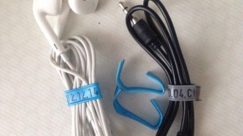 Kabel und Kopfhörer sind ordentlich mit Halterungen zusammengebunden und liegen auf einer hellen Oberfläche.