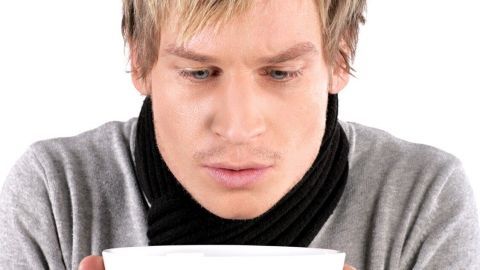 Ein Mann in einem grauen Pullover und Schal hält eine weiße Schüssel in den Händen und sieht nachdenklich hinein.