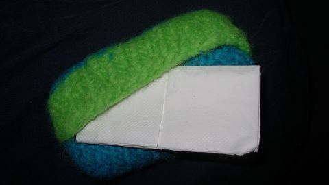 Eine gefilzte Taschentüchertasche liegt auf einem dunklen Untergrund und hält ein paar Taschentücher sicher.