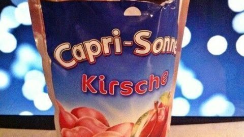 Ein Löffel mit frischem Capri-Sonne Slush steht über einem Becher, umgeben von bunten Lichtern im Hintergrund.