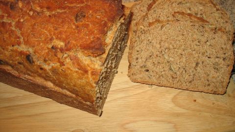 Ein frisch gebackenes Dinkel-Vollkorn-Brot liegt auf einem Holzbrett, neben einer geschnittenen Scheibe.
