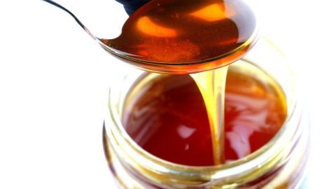 Ein Löffel mit goldbraunem Manuka-Honig schwebt über einem offenen Glas, das die gesunde Süßigkeit enthält.