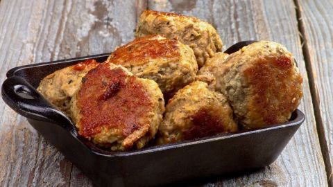 Kräuterfrikadellen liegen appetitlich in einer schwarzen Schale und sind knusprig gebraten auf rustikalem Holzuntergrund.