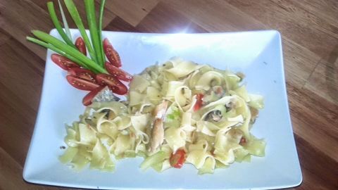 Pasta mit Heringsfilet wird auf einem weißen Teller mit frischen Zutaten und grünen Zwiebeln präsentiert.