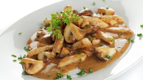 Zarte Stücke von Geschnetzeltem vom Schwein in einer cremigen Sauce, garniert mit frischer Petersilie auf einem weißen Teller.