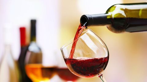 Ein Rotwein wird aus einer offenen Flasche in ein elegantes Glas eingeschenkt, umgeben von weiteren Weinen im Hintergrund.